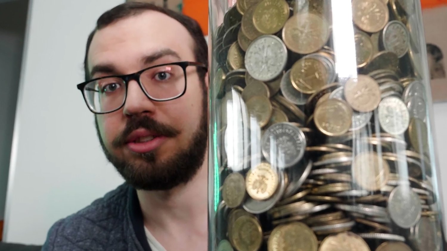 Słój pełen drobnych monet PLN. Mężczyzna w tle.