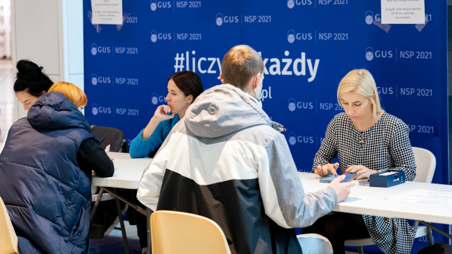 kolejka do spisu powszechnego, ludzie siedzą przy stoliku i uzupełniają dane w spisie powszechnym z konsultantem