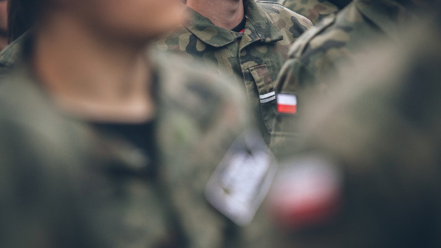polscy wojskowi idą przed siebie w mundurach z flagą Polski