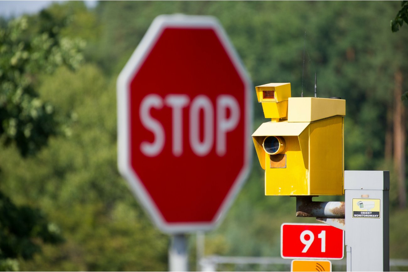 żółty fotoradar na tle lasu i czerwonego znaku stop