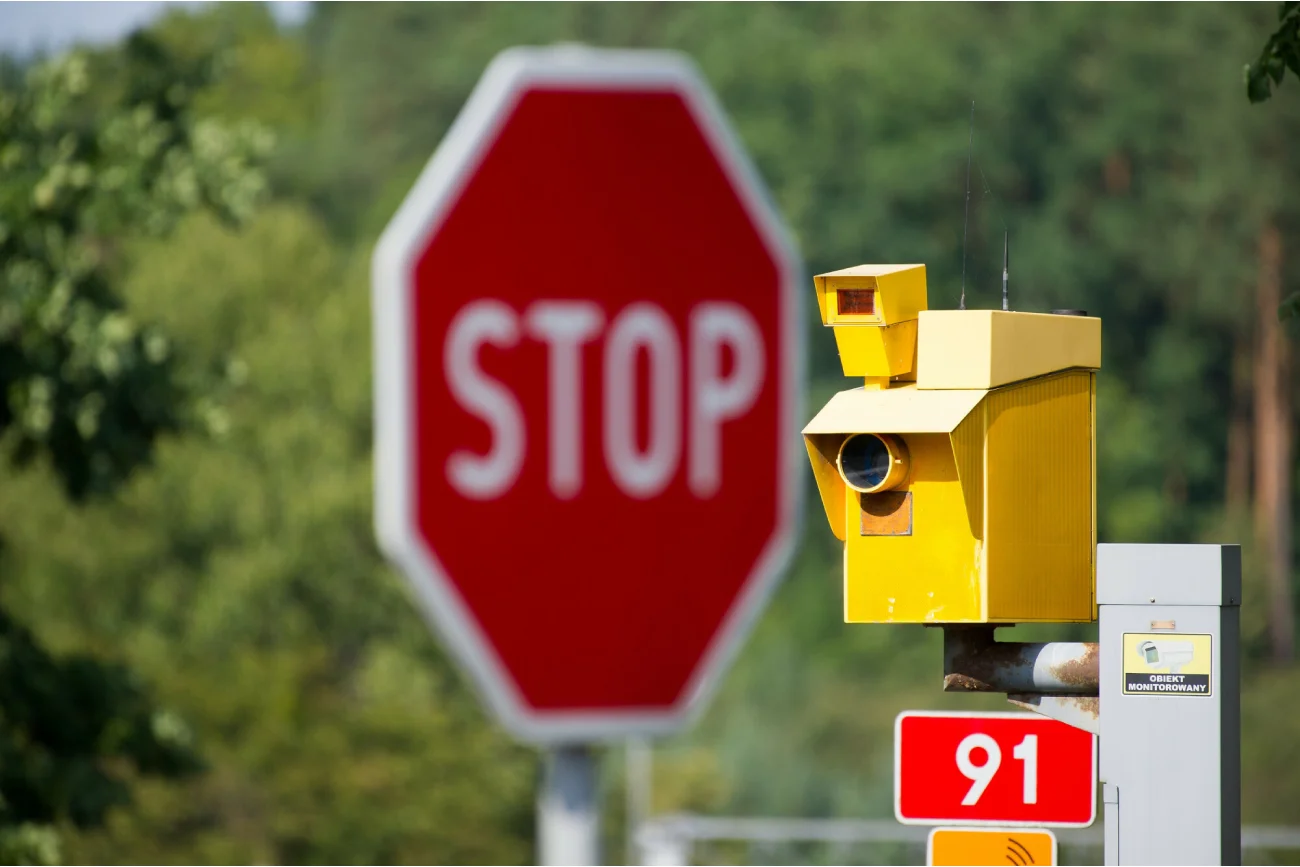 żółty fotoradar na tle lasu i czerwonego znaku stop