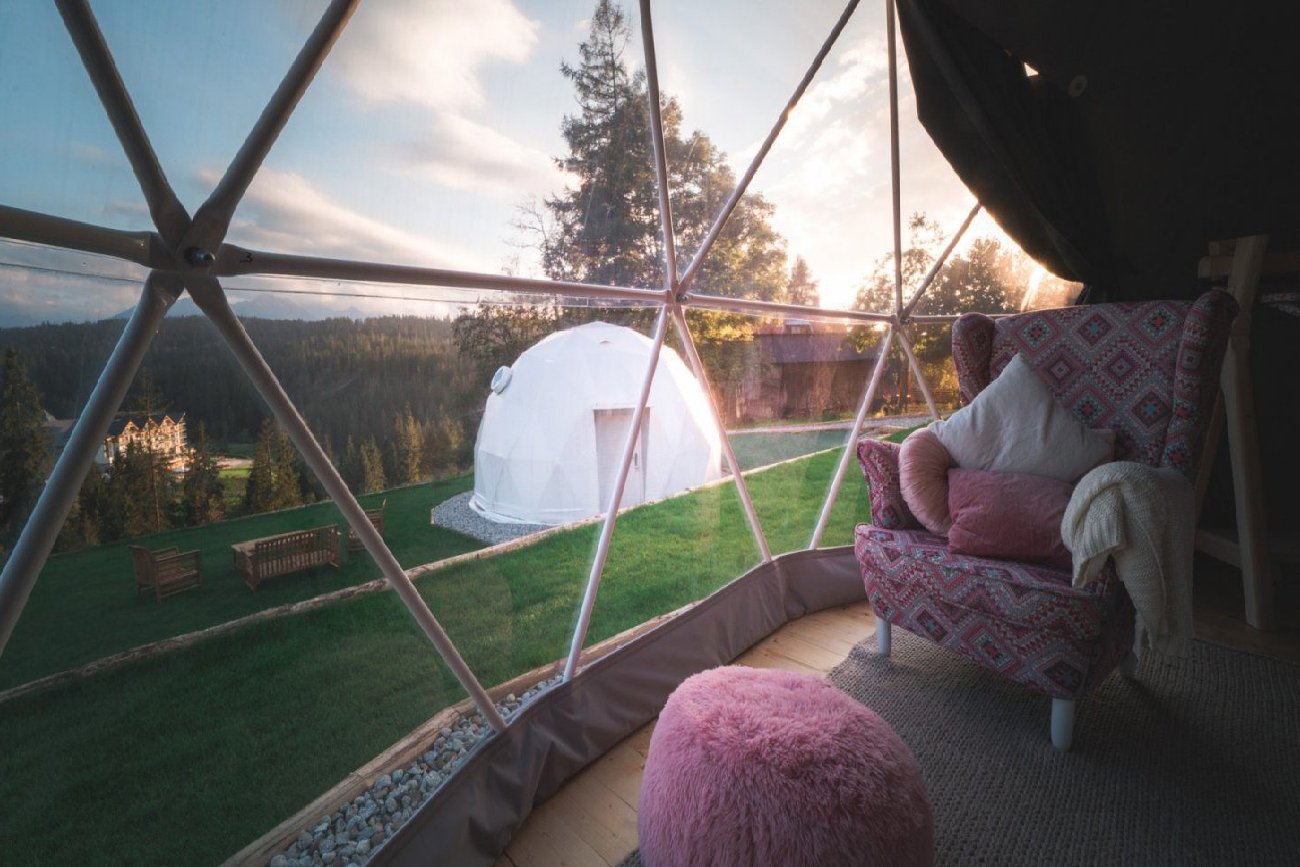 Kapsuła sferyczna widziana zza szyby pokoju, w której stoi różowy fotel i różowa pufa