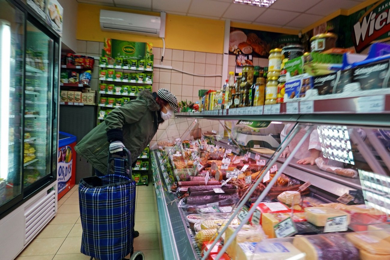 Starsza kobieta w maseczce robiaca zakupy w sklepie miesnym.