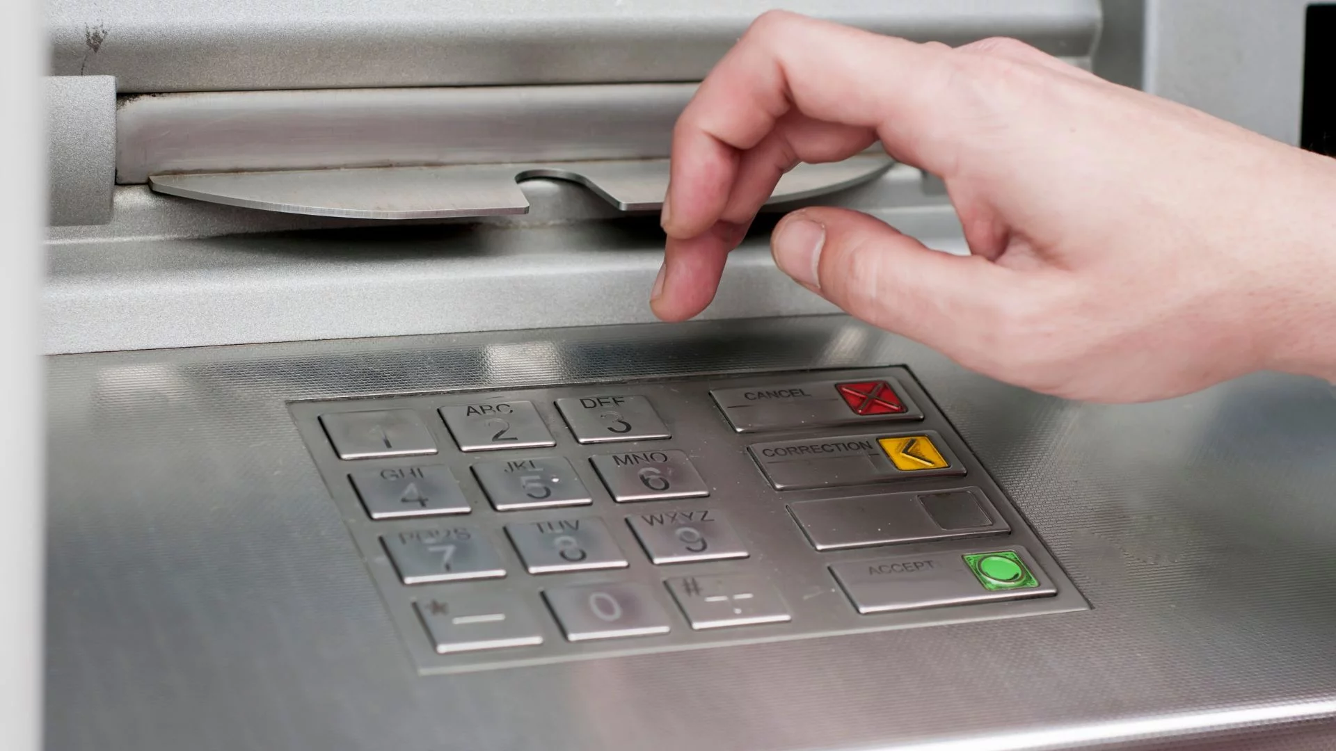 Mężczyzna używający bankomatu. UE chce przepisów ułatwiających wypłatę gotówki w sklepach.