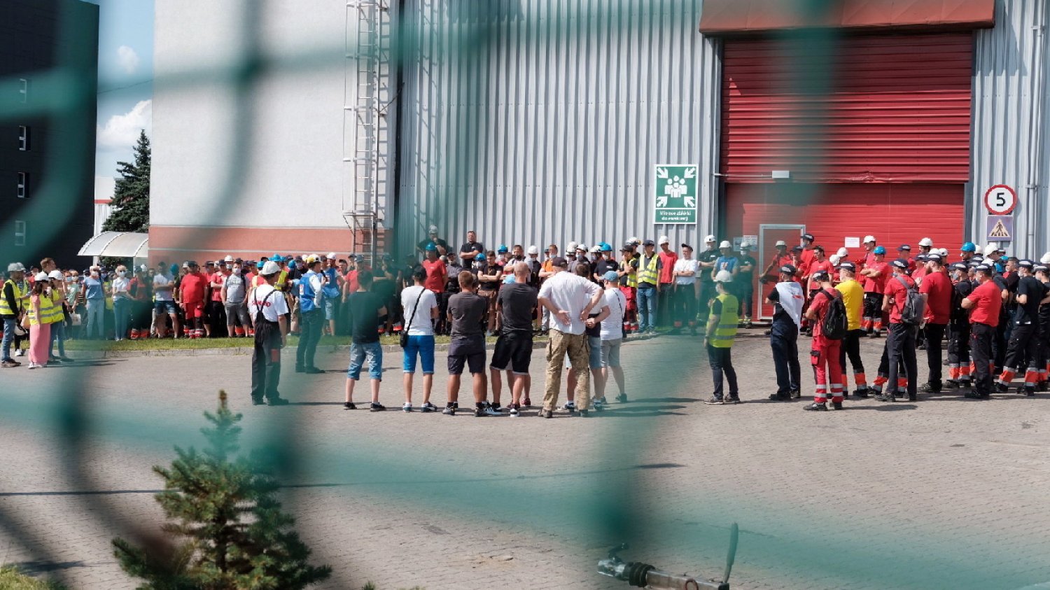 grupa mężczyzn ubrana w odzież roboczą podczas strajku za zieloną siatką