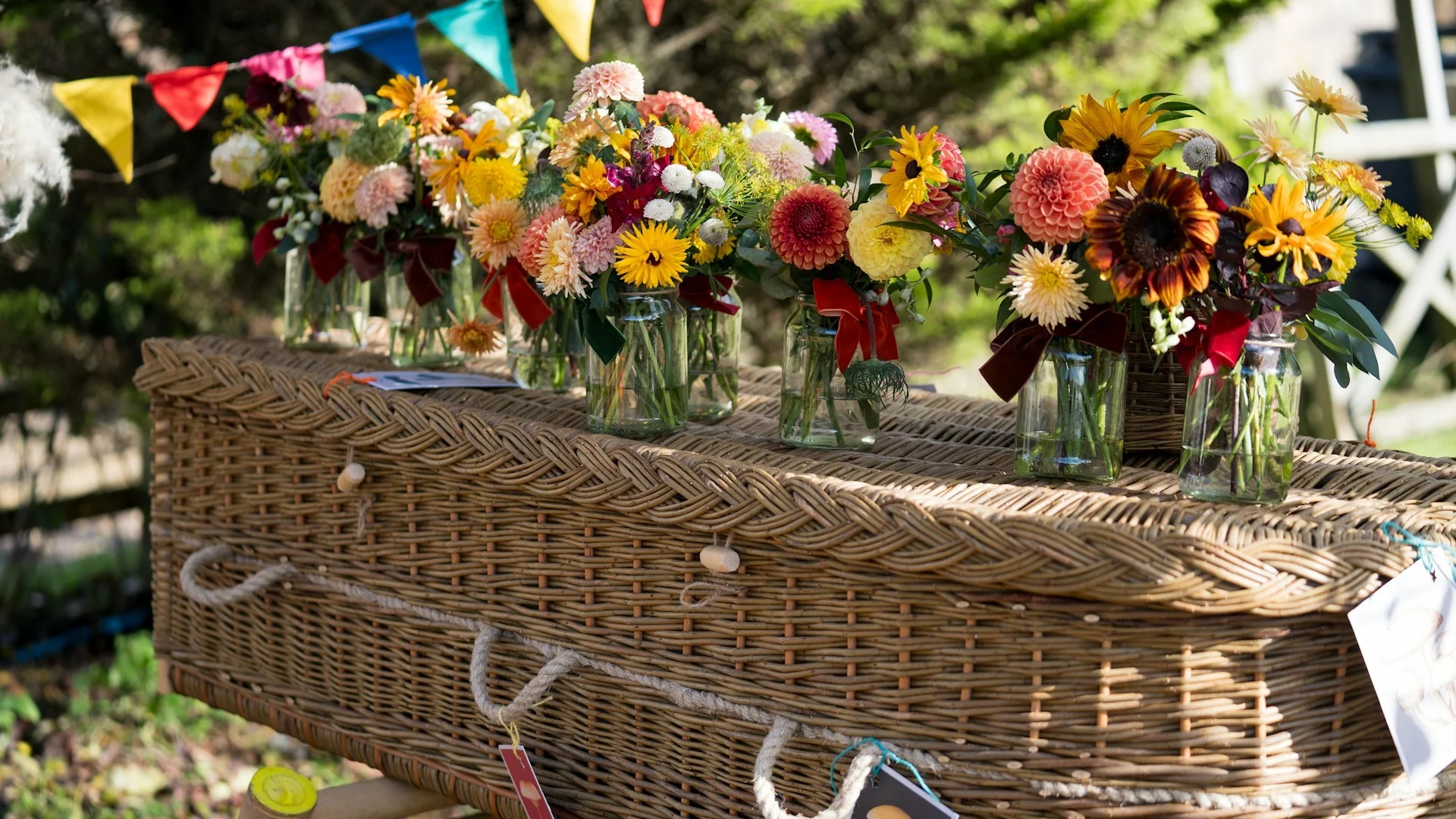Trumna z wikliny, a na niej wazony z kwiatami różnych gatunków.