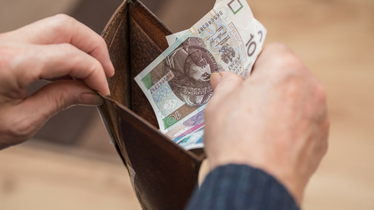 męska dłoń wkłada polskie banknoty pieniądze do portfela