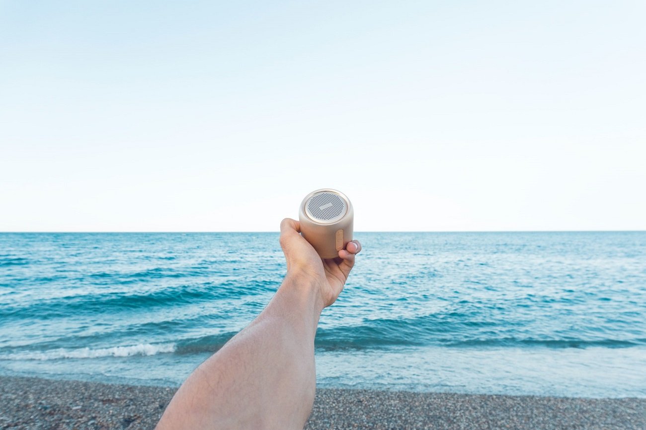 Osoba na plaży trzyma w wyciągniętej ręce głośnik.