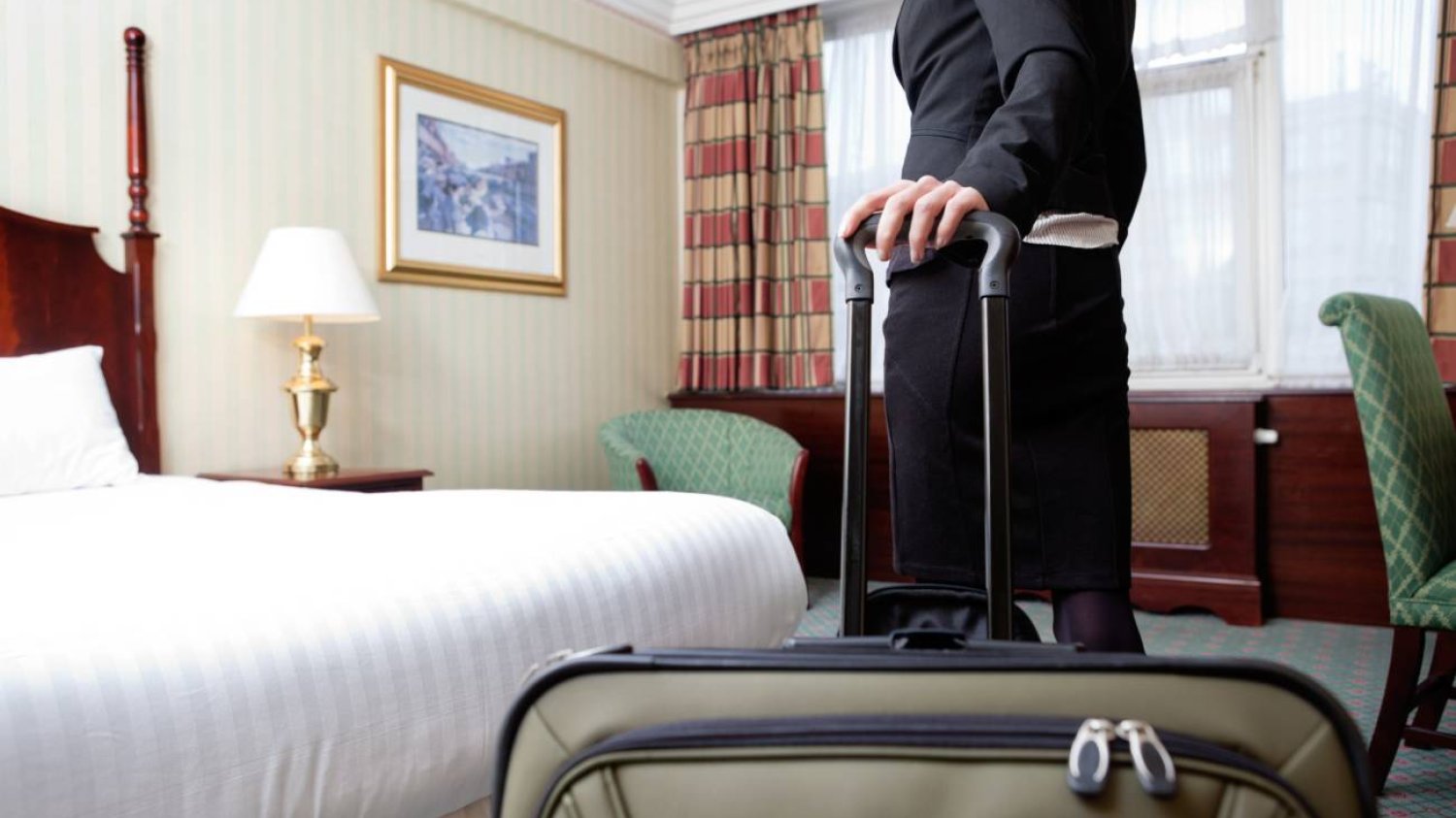 Pokój hotelowy. Kobieta z walizką przy łóżku.