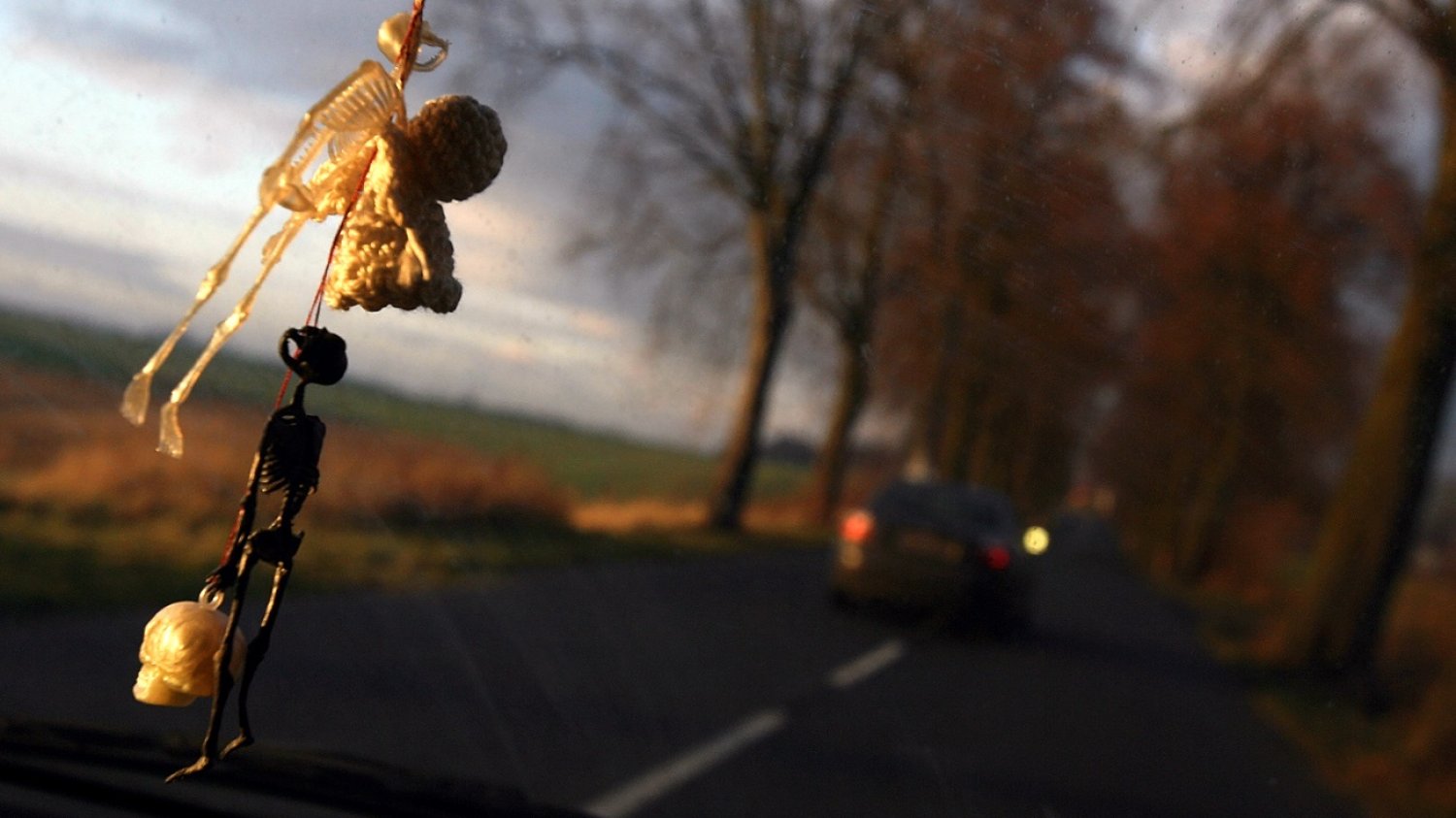 Przednia szyba samochodu. Przed maską wyprzedzający pojazd. Z lusterka zwisają breloki - kościotrupy.