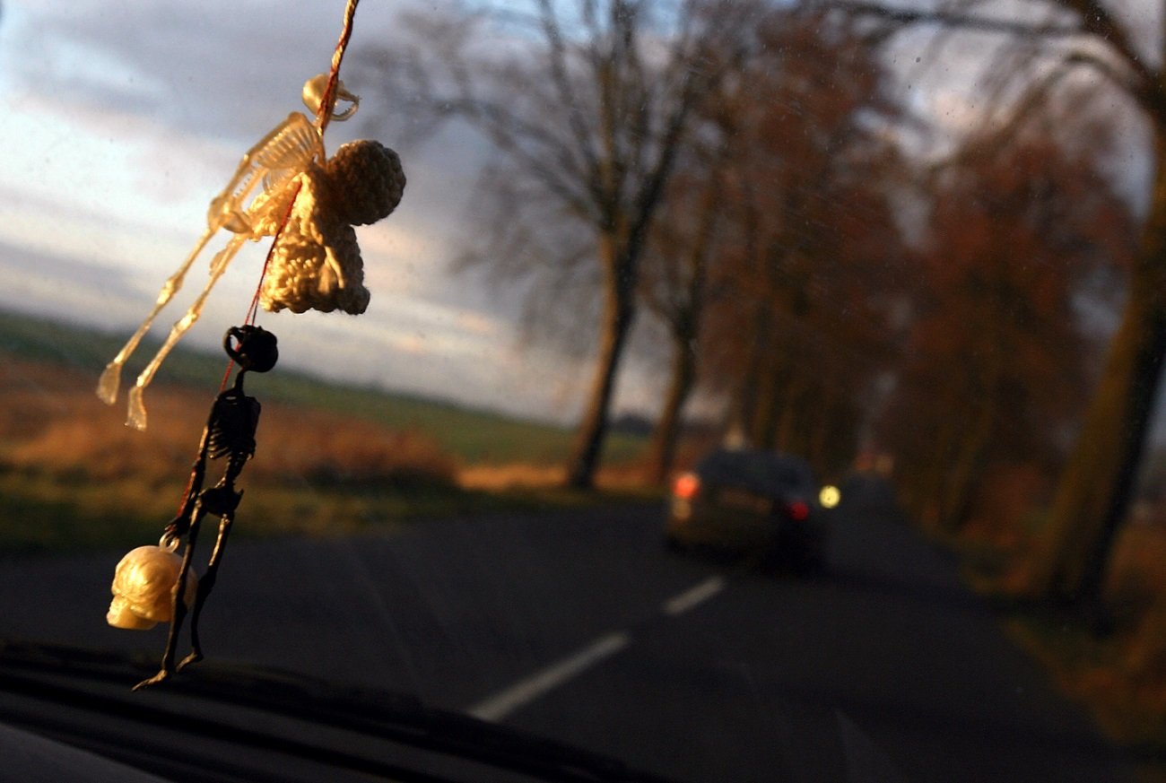 Przednia szyba samochodu. Przed maską wyprzedzający pojazd. Z lusterka zwisają breloki - kościotrupy.