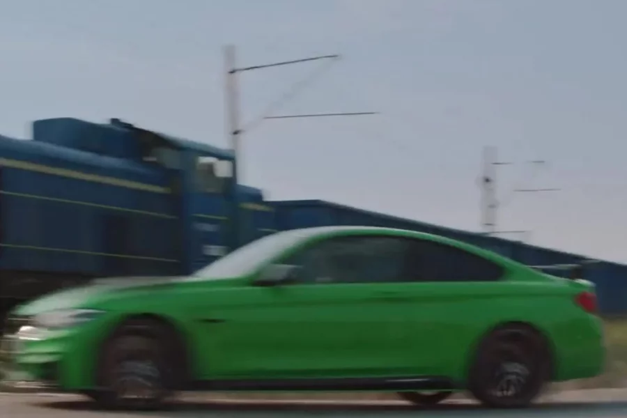 Kadr z kontrowersyjnej reklamy BMW: kierowca sportowej limuzyny dogania pociąg tuż przed przejazdem.