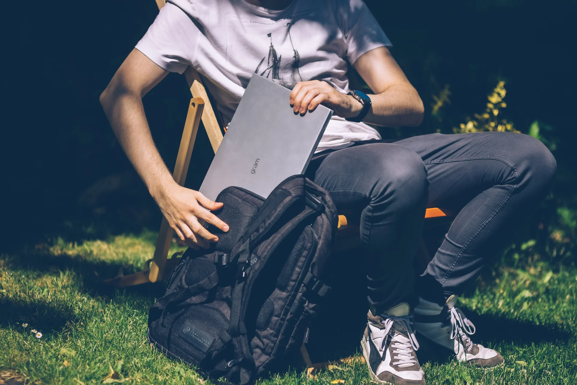 Laptop LG Gram. Siedzący na leżaku mężczyzna wkłada go do plecaka.