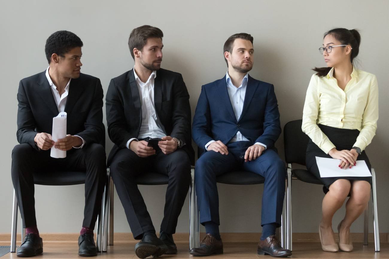 Kobieta i kilku mężczyzn na rozmowie o pracę. Ona przerażona, oni łypią ze złością.