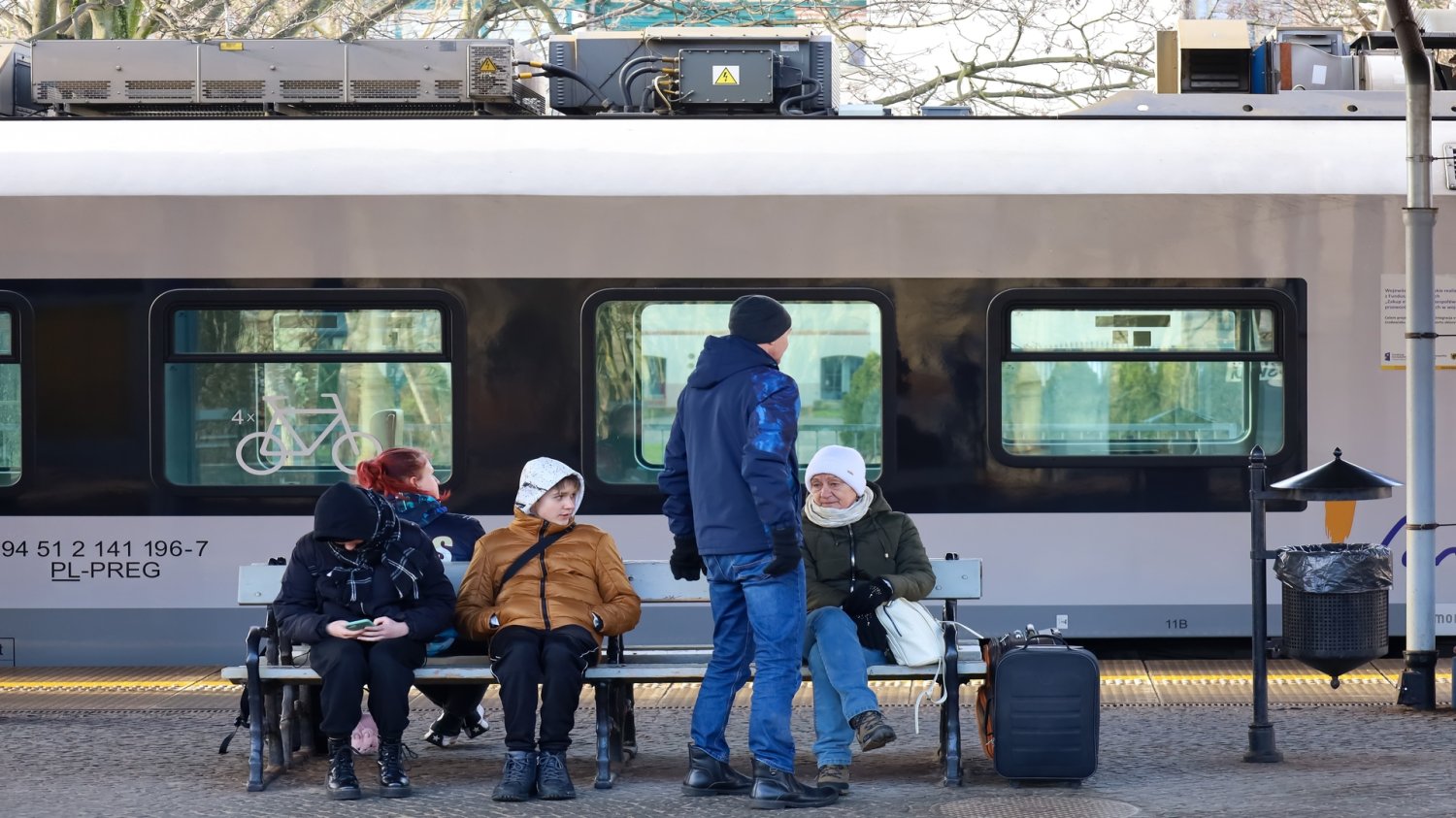 Pakt Kolejowy podpisany. "To życzliwość dla Kujawsko-Pomorskiego" – pisze jedna z internautek. Grupka ludzi ubrana w kurtki, którzy czekają na peronie kolejowym.