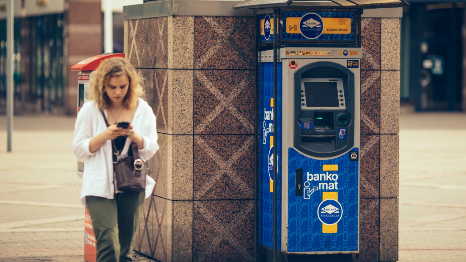 Kobieta przechodząca obok bankomatu.