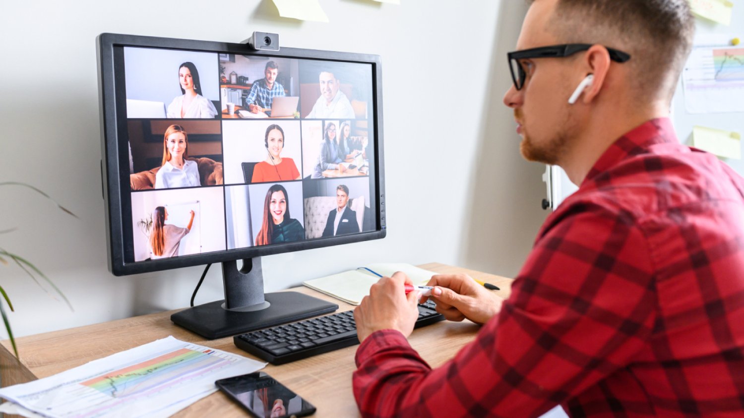 Spotkanie online młodego biznesmena z podwładnymi. Widok z boku na młodego mężczyznę rozmawiającego przez kamerę internetową z grupą ludzi w miejscu pracy