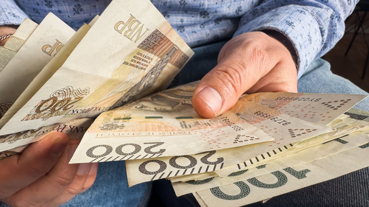 Człowiek trzymający w dłoniach banknoty 200 zł. Bezpieczeństwo finansowe w dobie kryzysu. Europejskie banki zalecają "gotówkową poduszkę".