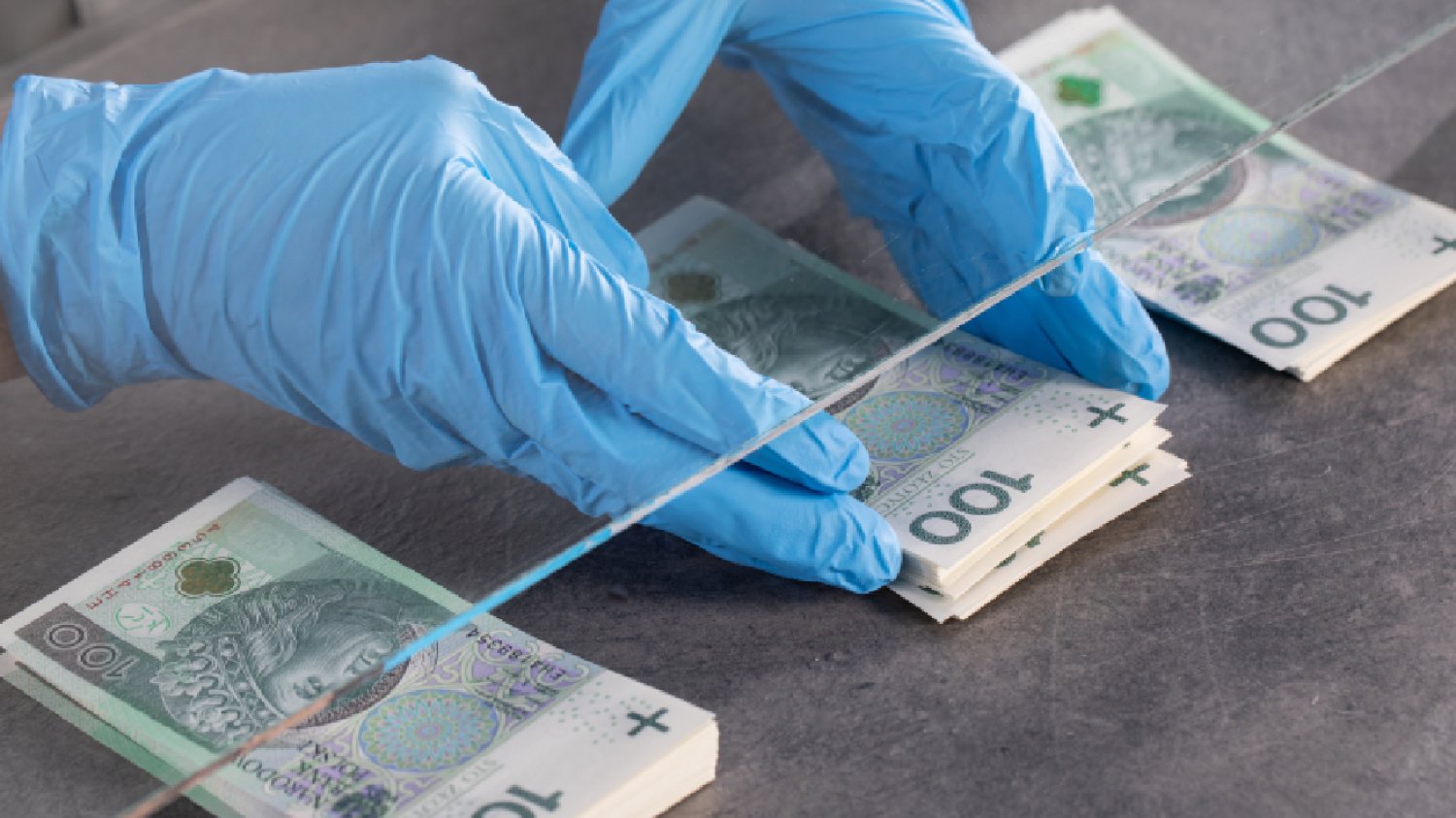 człowiek w niebieskich rękawiczkach liczby banknoty sto złotych na ladzie pod szklaną szybą