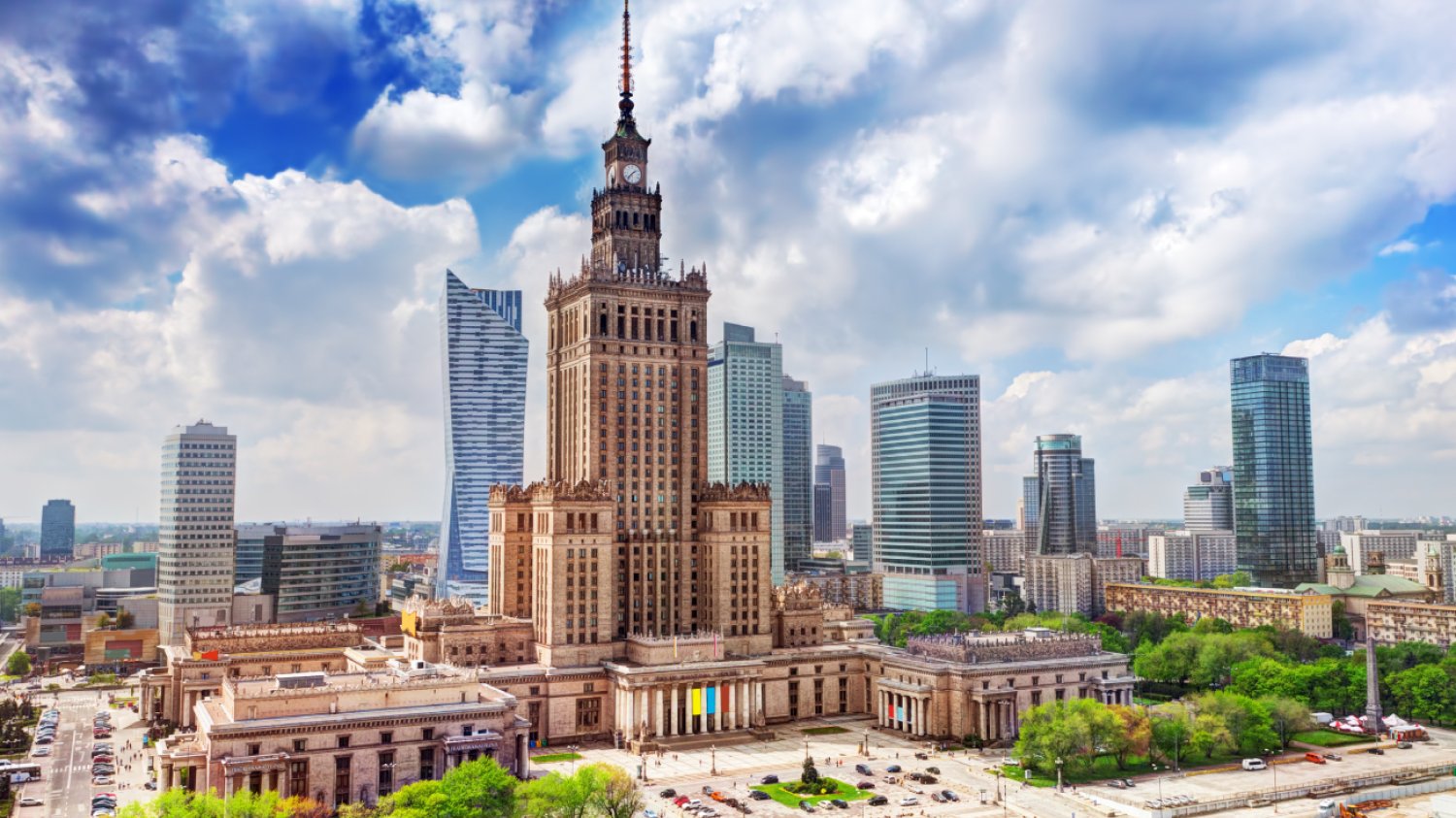 Zdjęcie centrum Warszawy w słoneczny dzień: na pierwszym planie Pałac Kultury i Nauki, w tle wieżowce.