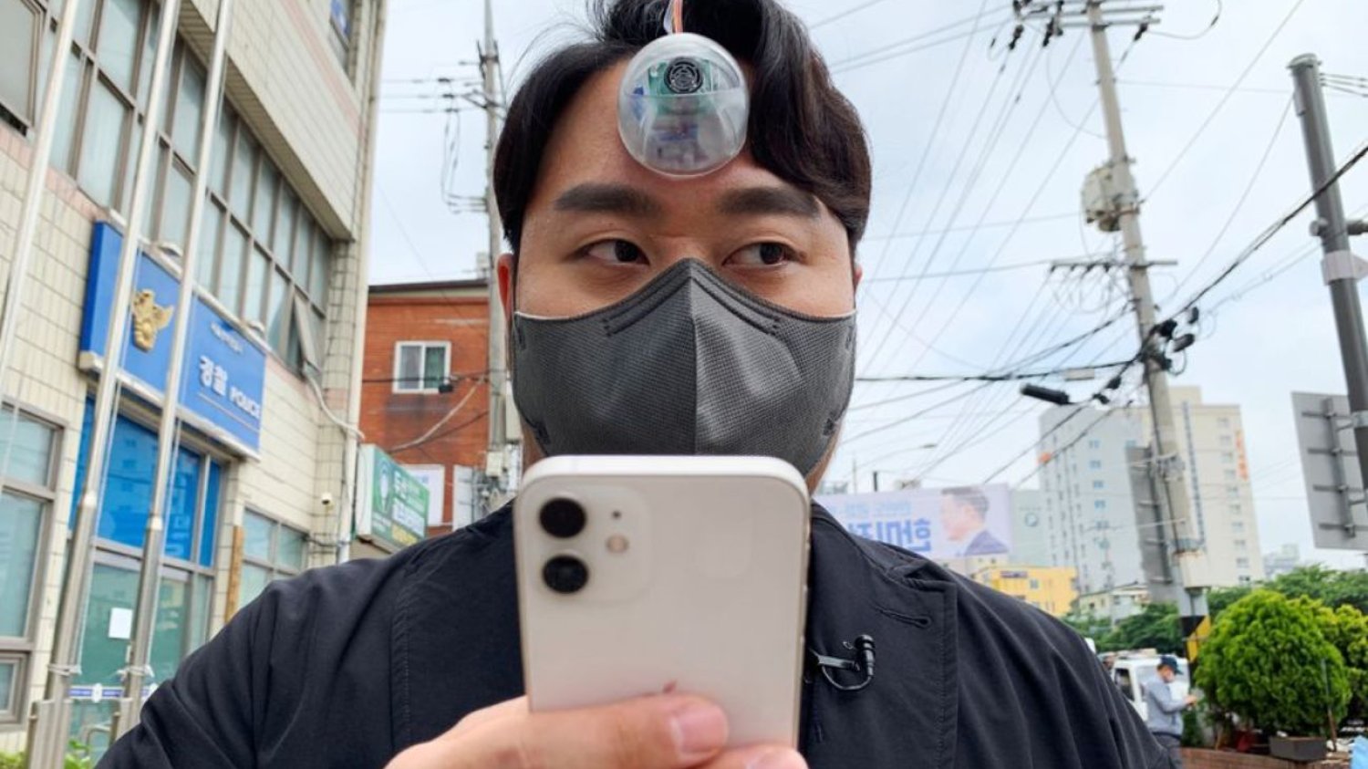 Koreański inżynier Paeng Min-wook z kamerą "The Third Eye" na czole i smartfonem w ręku.