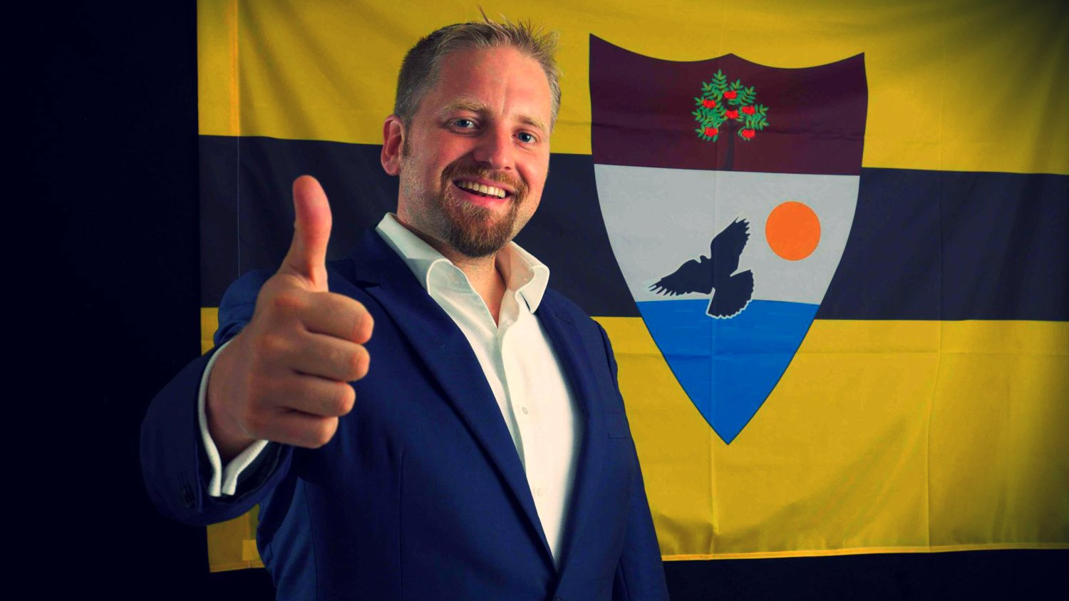 Vít Jedlička pozuje na tle flagi Liberlandu w sierpniu 2015, po tym jak pierwsi Liberlandczycy zasiedlili jego kraj
