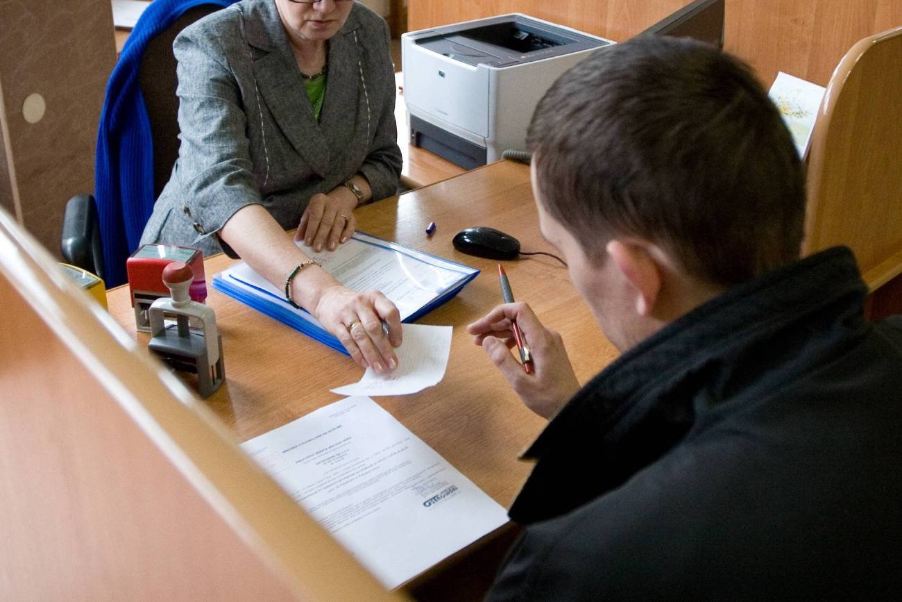 Urzędniczka publiczna obsługuje mężczyznę w urzędzie. Biurko z dokumentami.