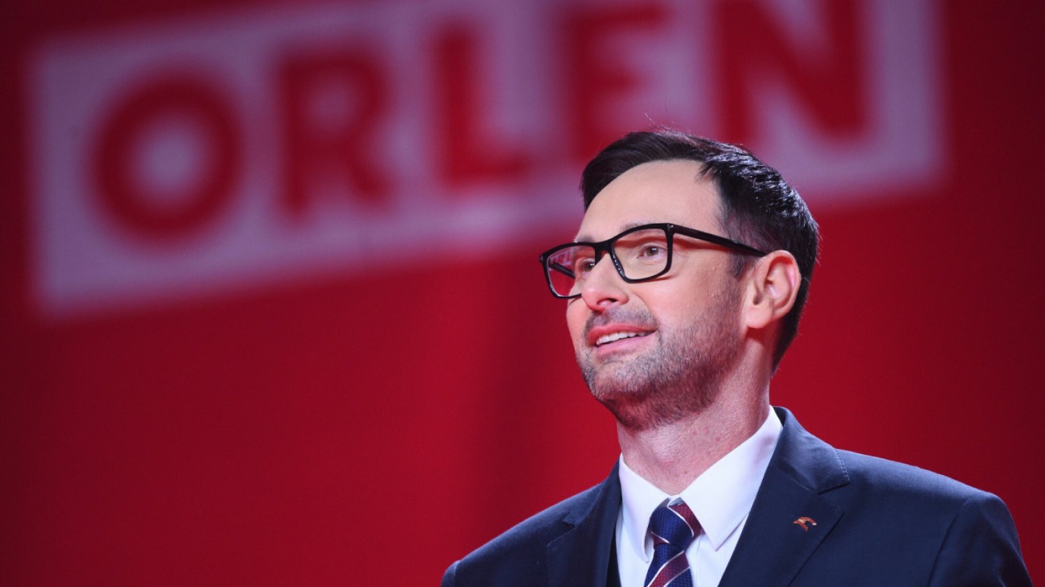 prezes Orlenu Daniel Obajtek na konferencji firmy stoi na czerwonym tle przed grupą dziennikarzy