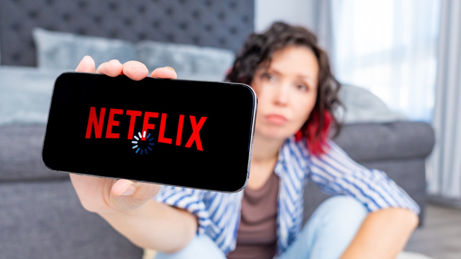 Kobieta trzyma telefon z uruchomionym Netflixem. Widoczne kółko ładowania filmu.