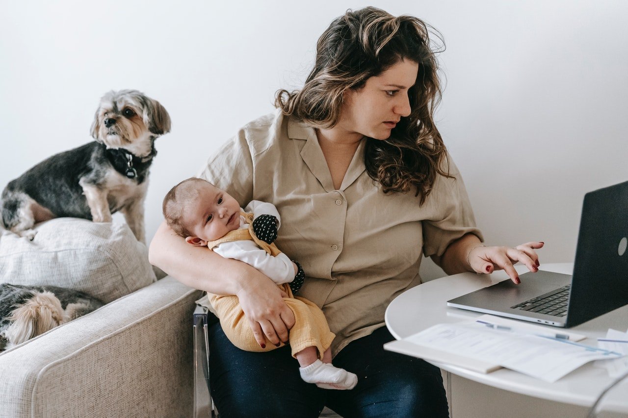 Home office - kobieta przy komputerze zajmuje się małym dzieckiem.