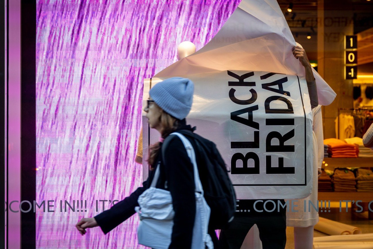 Kobieta przechodzi obok sklepu, w którym pracownik przykleja plakat "Black Friday" na wystawie sklepowej