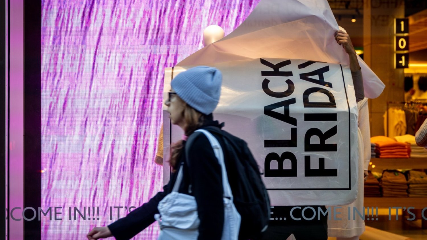 Kobieta przechodzi obok sklepu, w którym pracownik przykleja plakat "Black Friday" na wystawie sklepowej