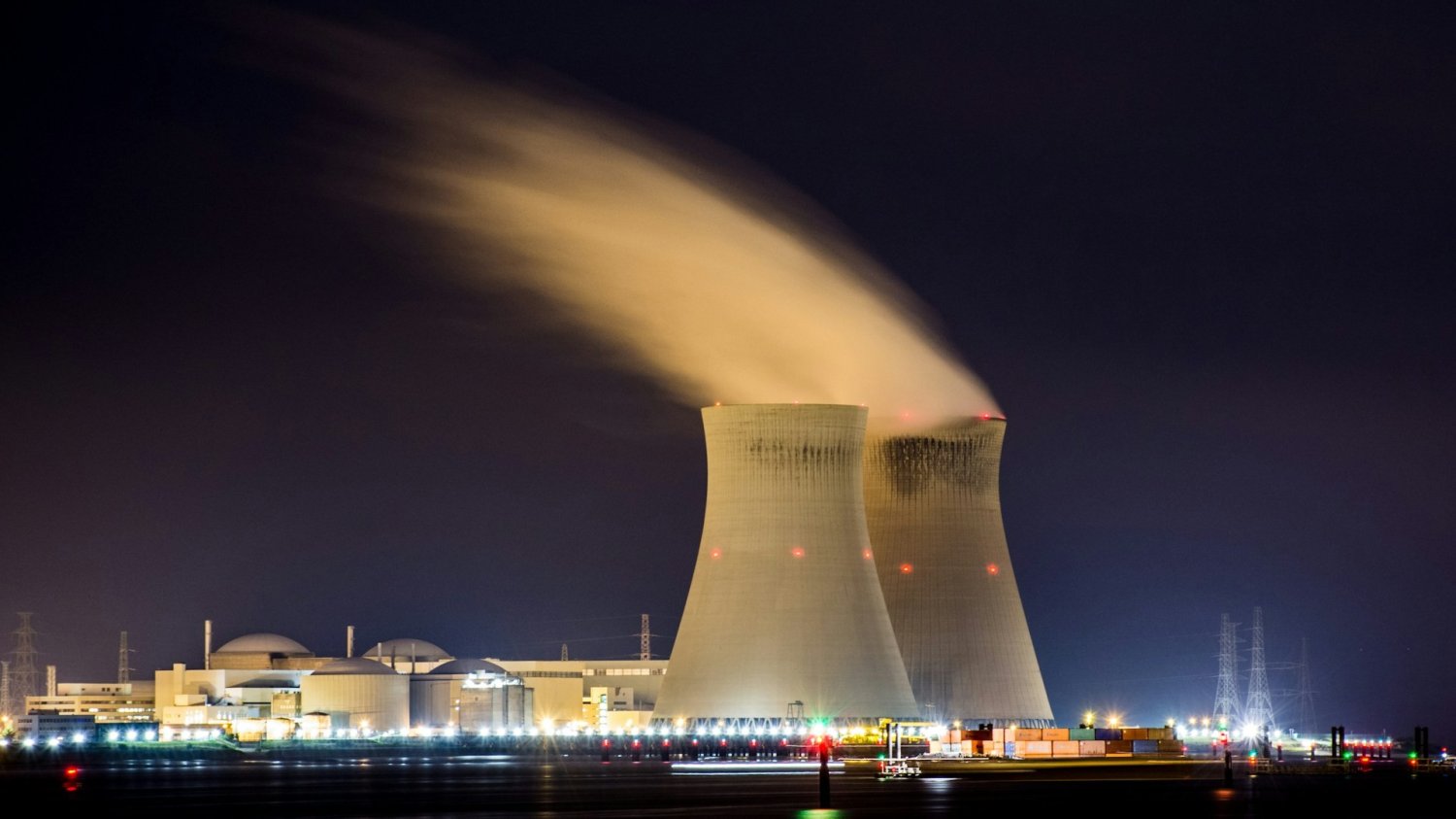 Elektrownia atomowa na tle miasta nocą: nad kominami unosi się dym. Niemcy likwidują, a Polska buduje elektrownię atomową.