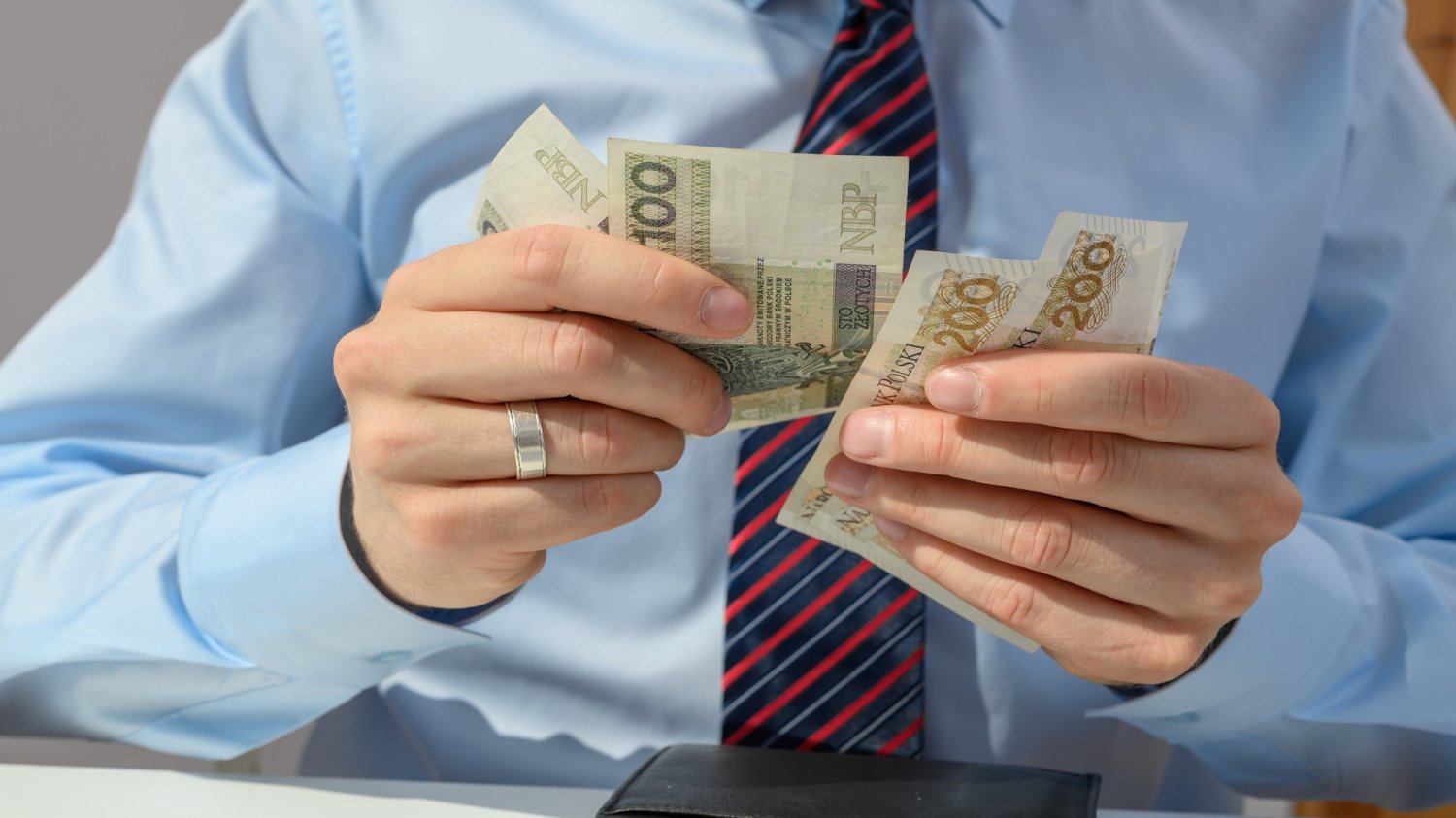 Banknoty w rękach człowieka w koszuli i krawacie. Podziękujcie Unii. Szefowie muszą podnieść pensje lojalnym pracownikom.