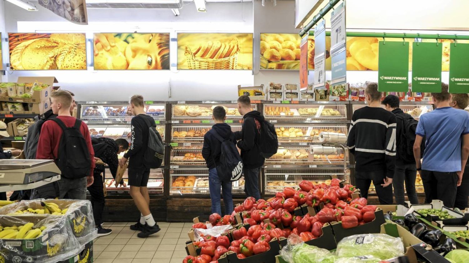 Wnętrze sklepu spożywczego, klienci kupują towary. Na pierwszym planie pomidory, inne warzywa.