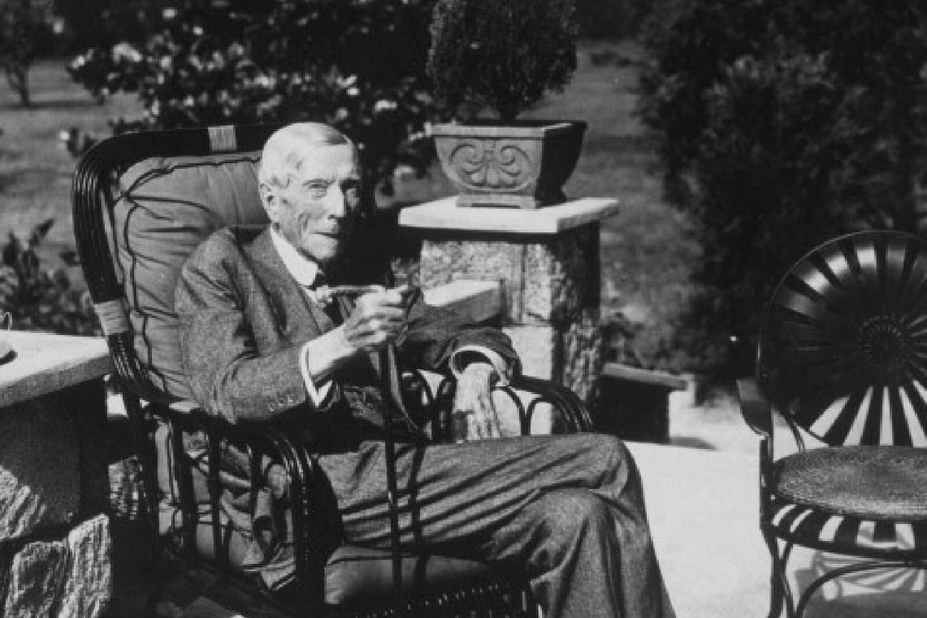 John Davison Rockefeller na czarno-białym zdjęciu retro siedzi w ogrodzie na fotelu ubrany w elegancki garnitur