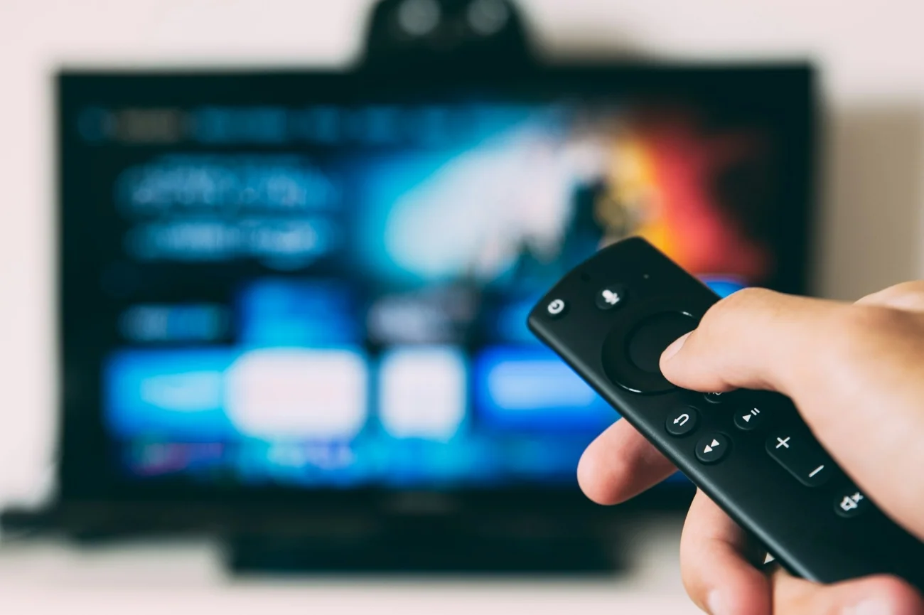 Niemiecka telewizja pod wrażeniem Polski. "Jak oni to robią?" Dłoń z pilotem skierowana w stronę ekranu włączonego telewizora.