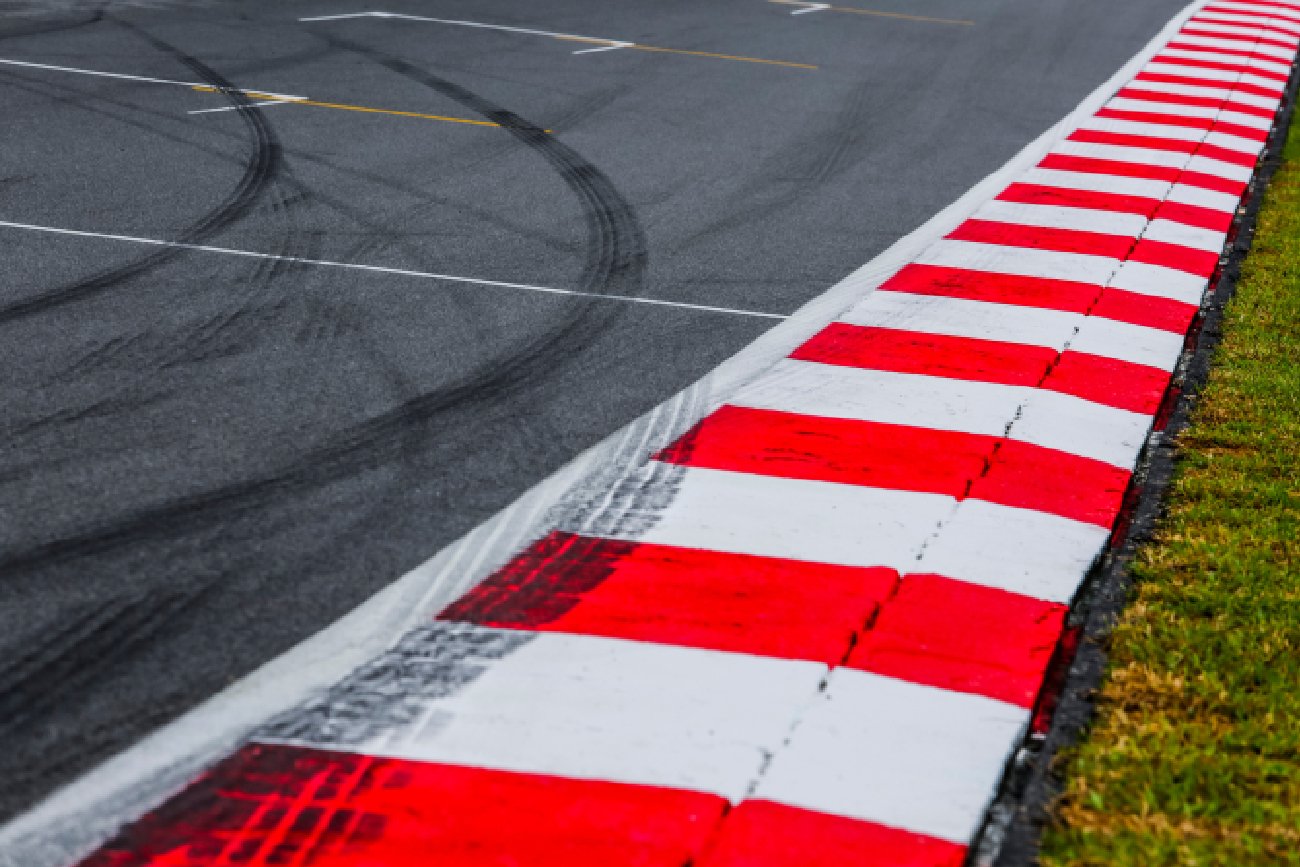 asfaltowy czerwono-biały krawężnik z detalem toru wyścigowego ze śladami opon, tor wyścigowy sportów motorowych z bliska.