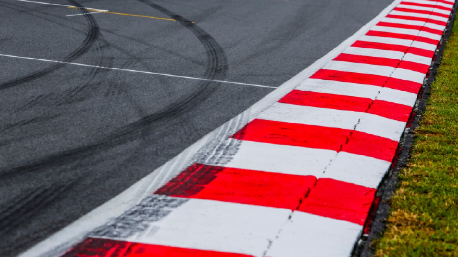asfaltowy czerwono-biały krawężnik z detalem toru wyścigowego ze śladami opon, tor wyścigowy sportów motorowych z bliska.