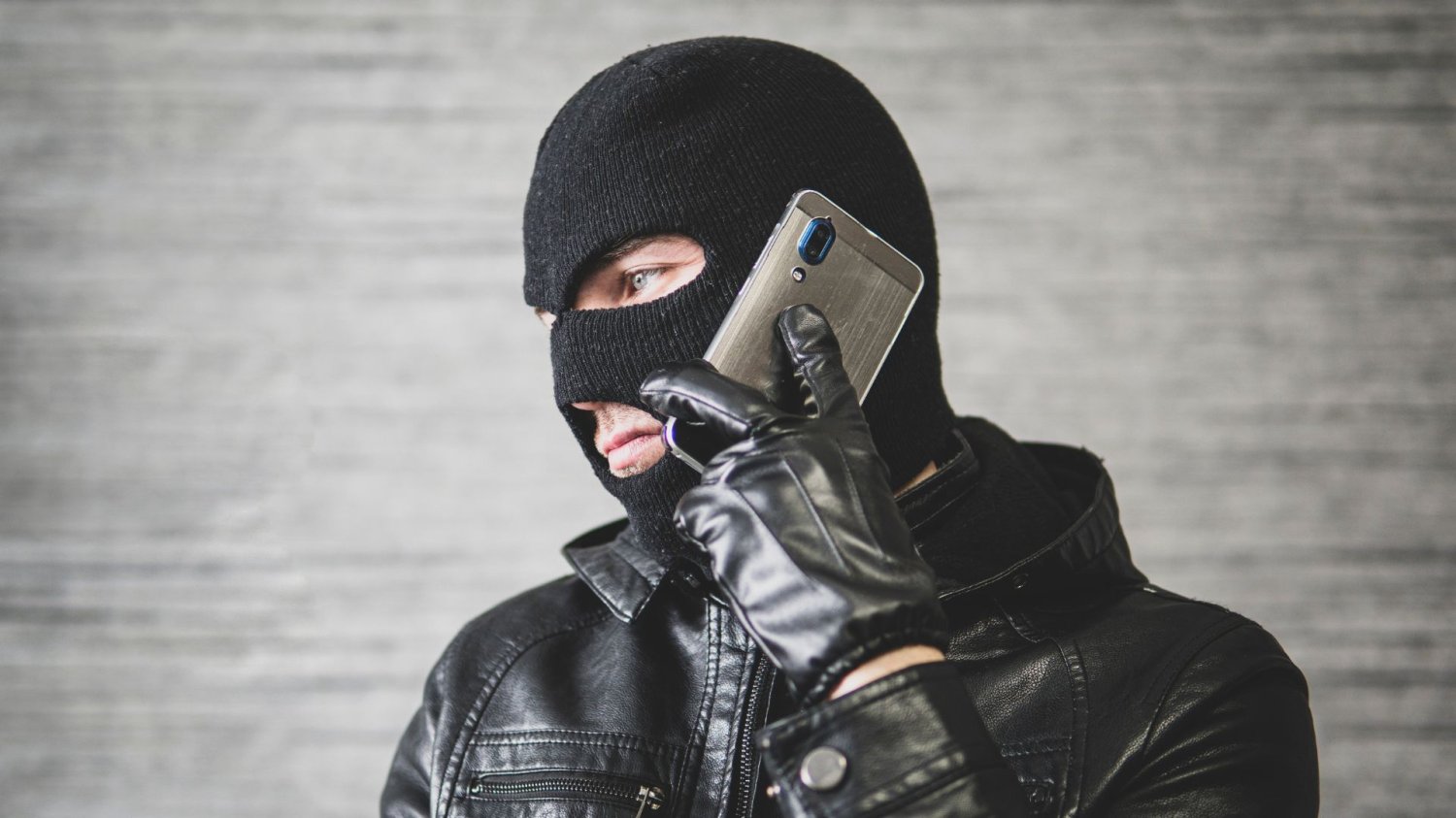 Człowiek w kominiarce używa telefony. Co trzeci Polak dostał taki telefon. Oszuści podszywają się pod urzędy i policje