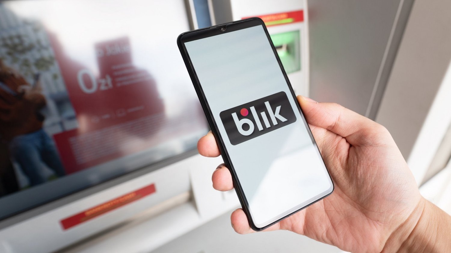 Płatność BLIKIEM - telefon wyciągnięty w dłoni przed bankomatem.
