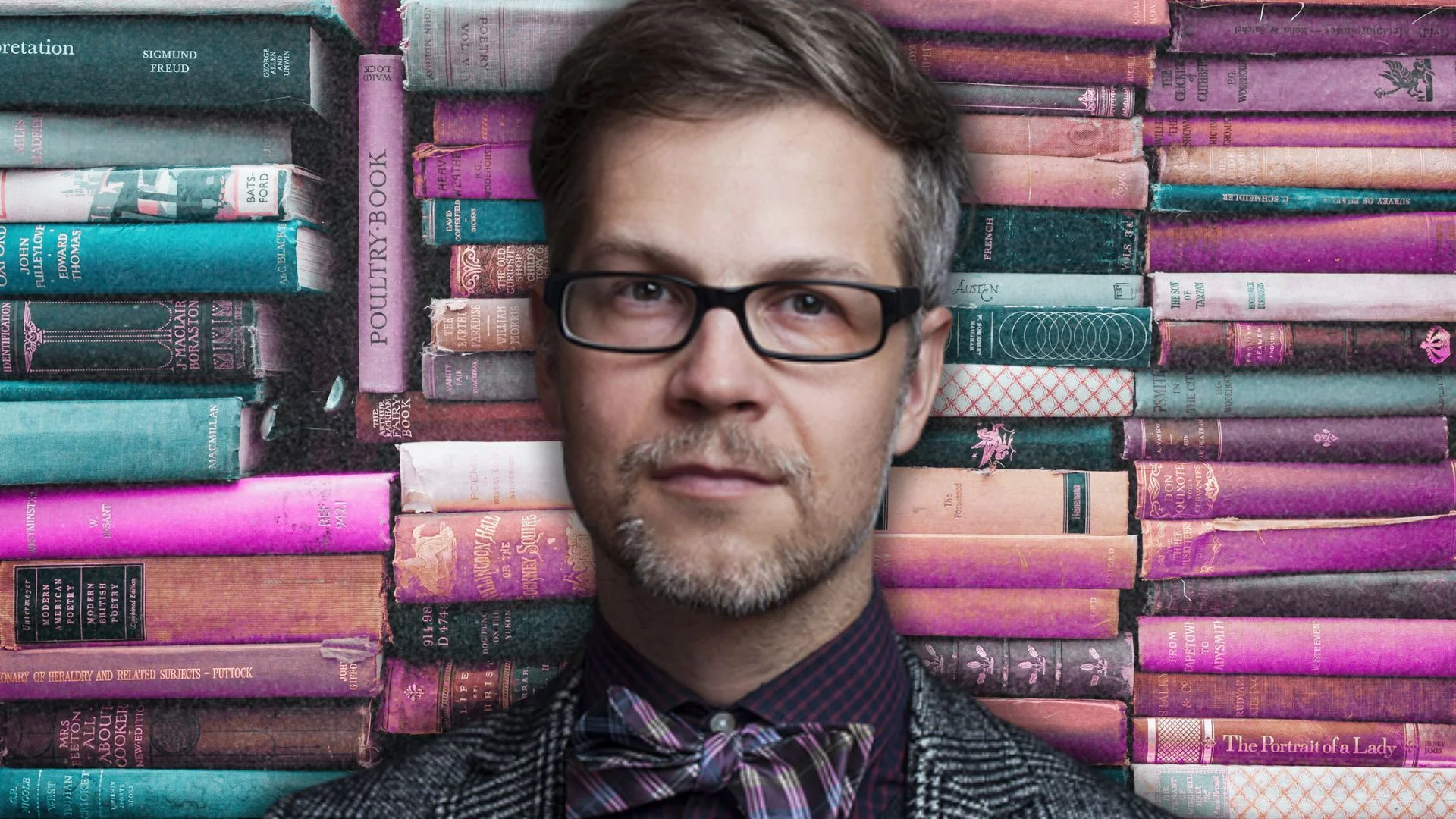 Mężczyzna w okularach stojący przed stertą książek.