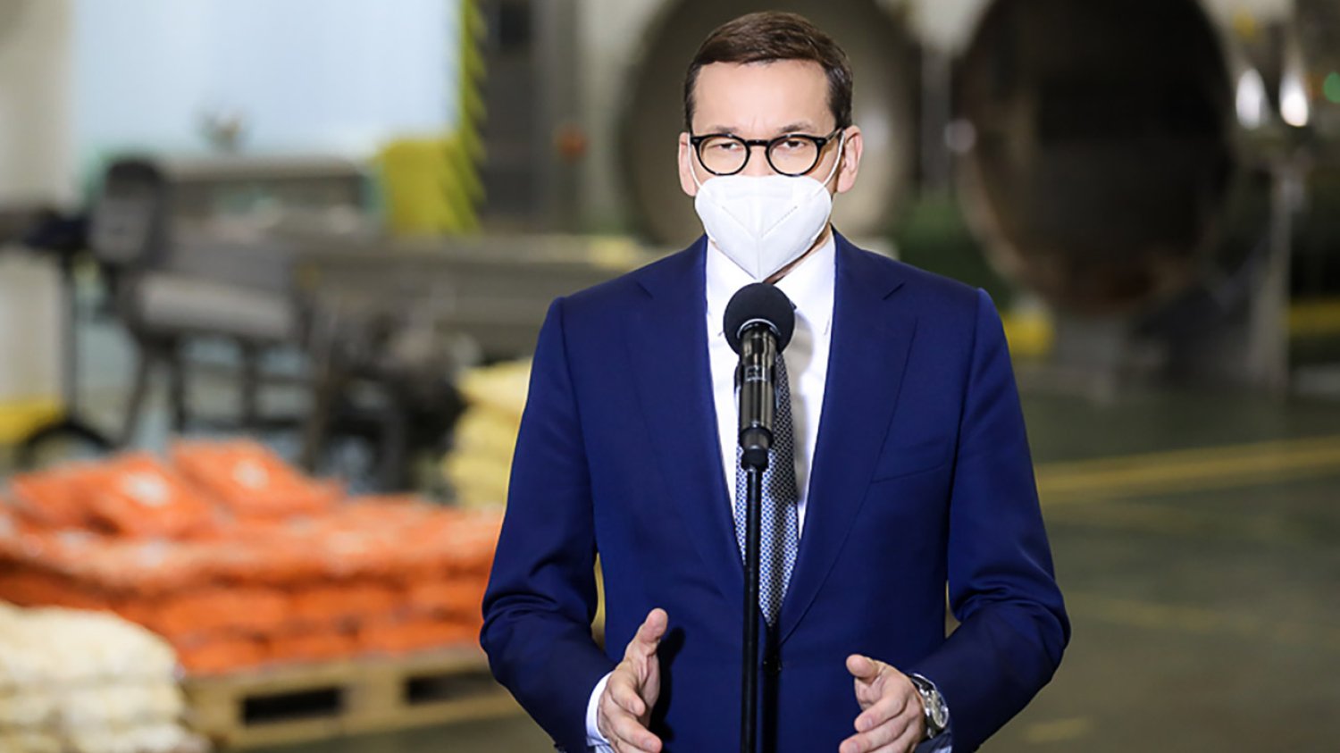 Premier Mateusz Morawiecki na tle zakładu przemysłowego.