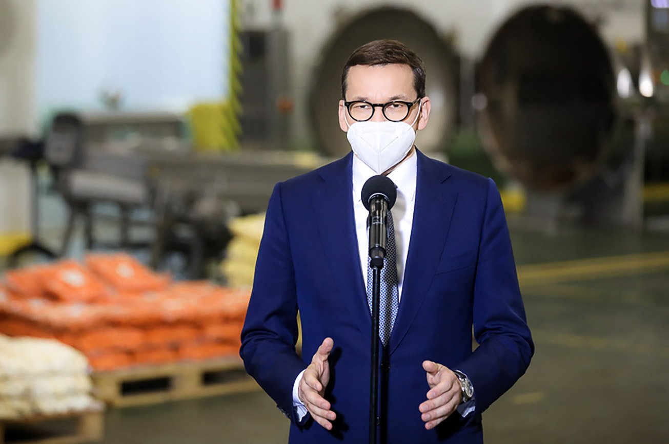 Premier Mateusz Morawiecki na tle zakładu przemysłowego.