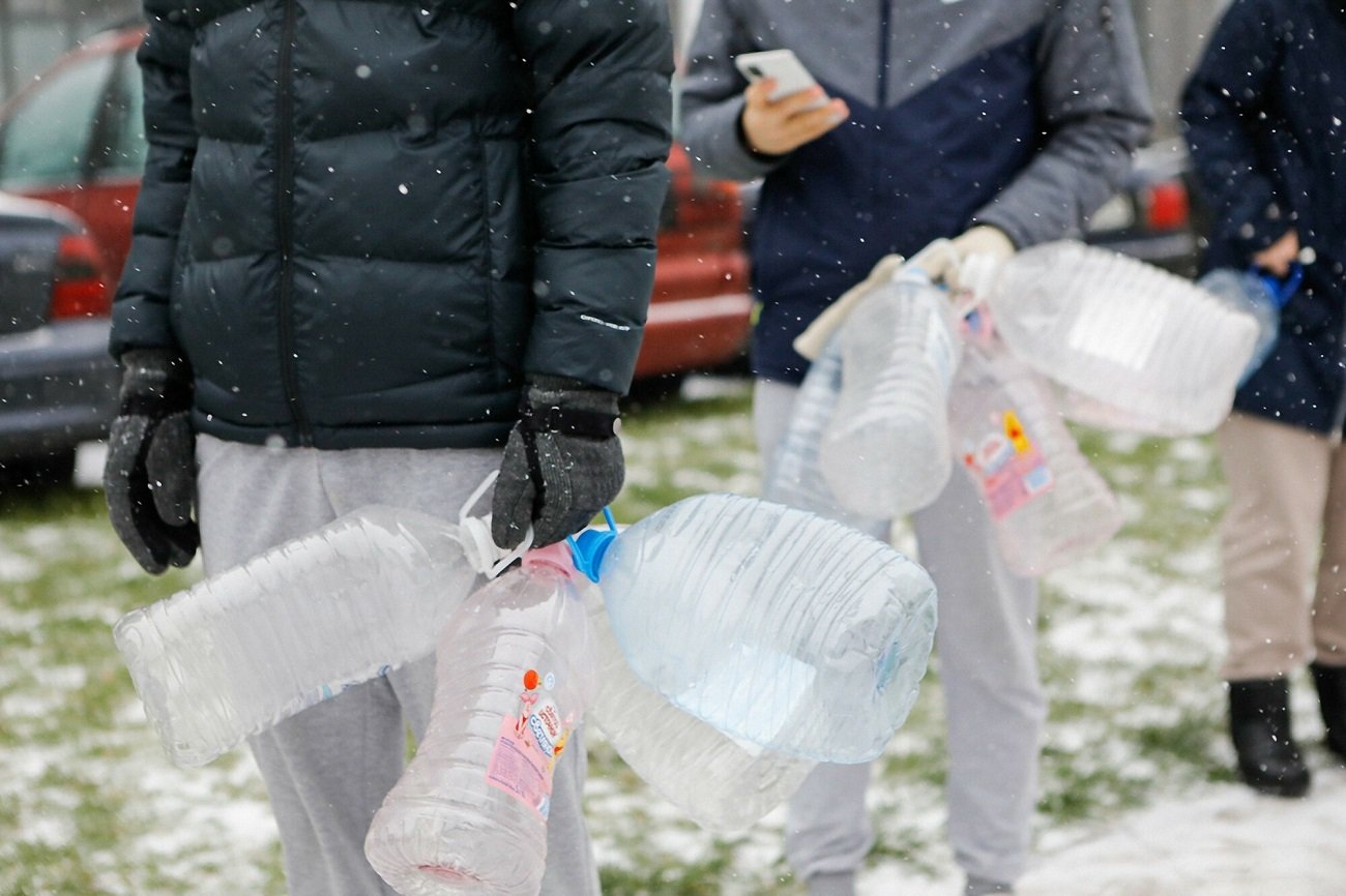 ludzie niosący plastikowe butle na wodę