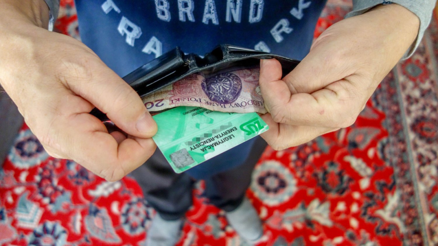 emeryt rencista trzyma w ręku legitymację ZUS i portfel z banknotem dwudziestozłotowym