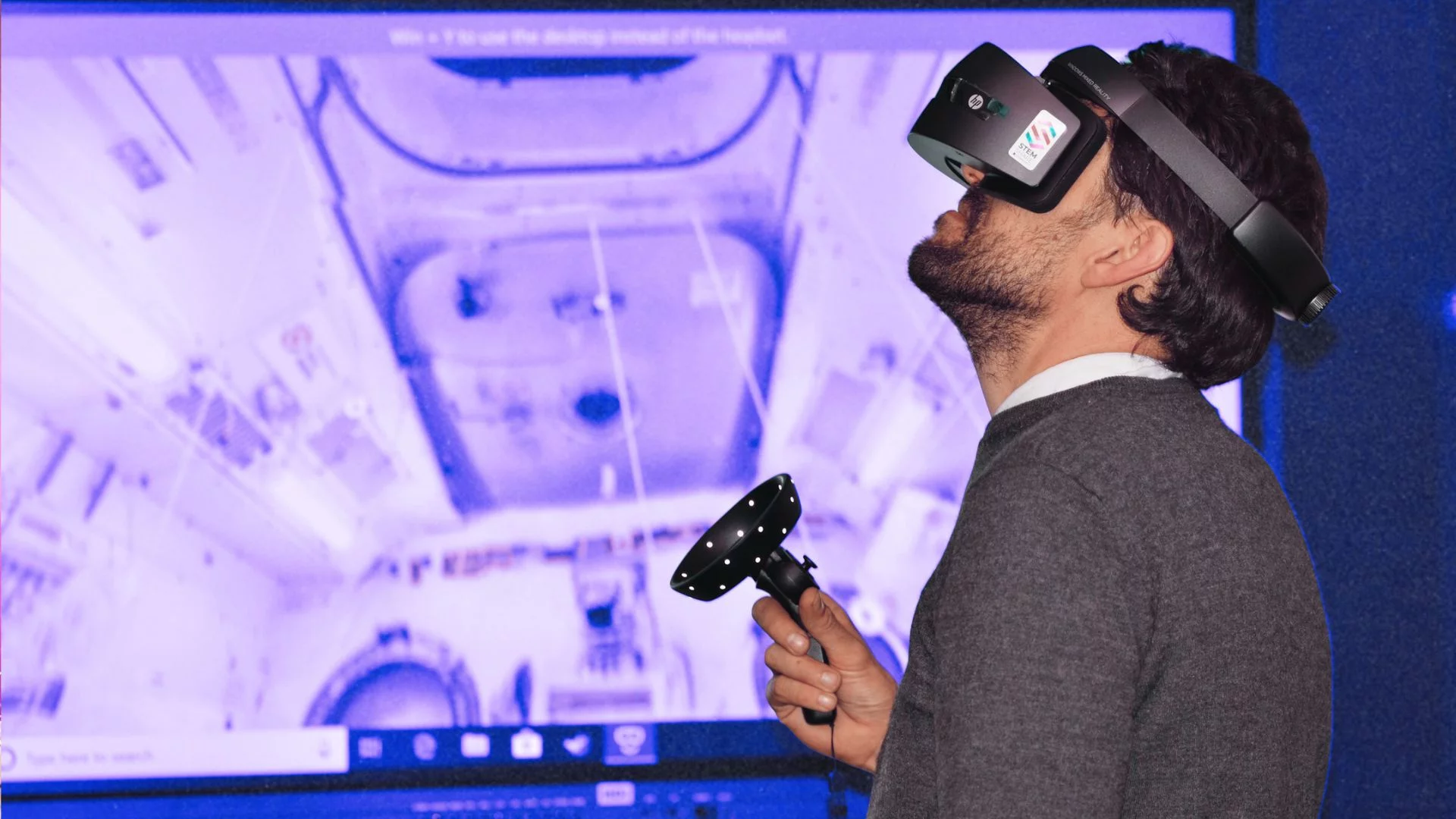 Mężczyzna w goglach VR stojący na tle ekranu.