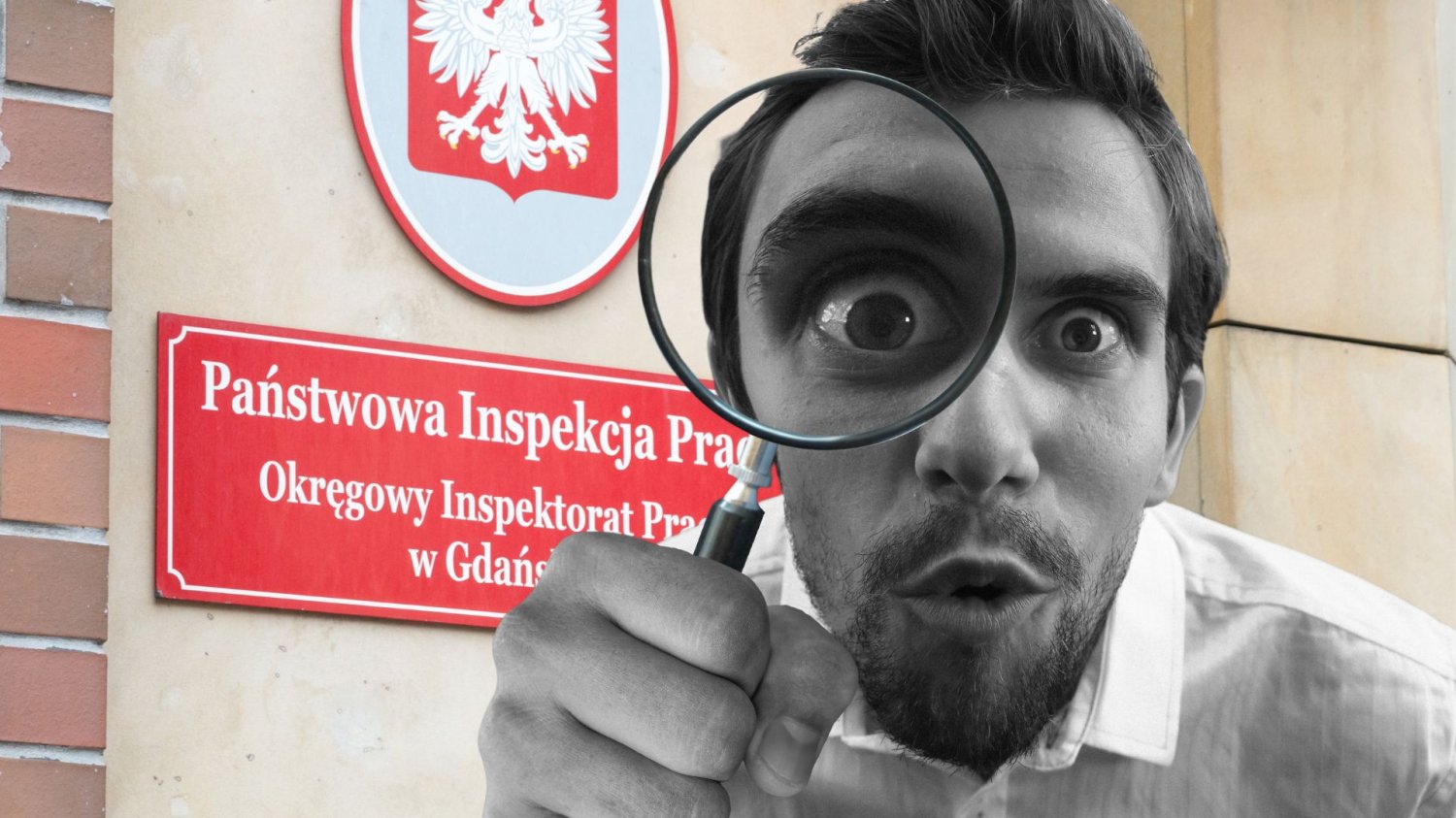 mężczyzna z lupą na tle tablicy inspekcji pracy