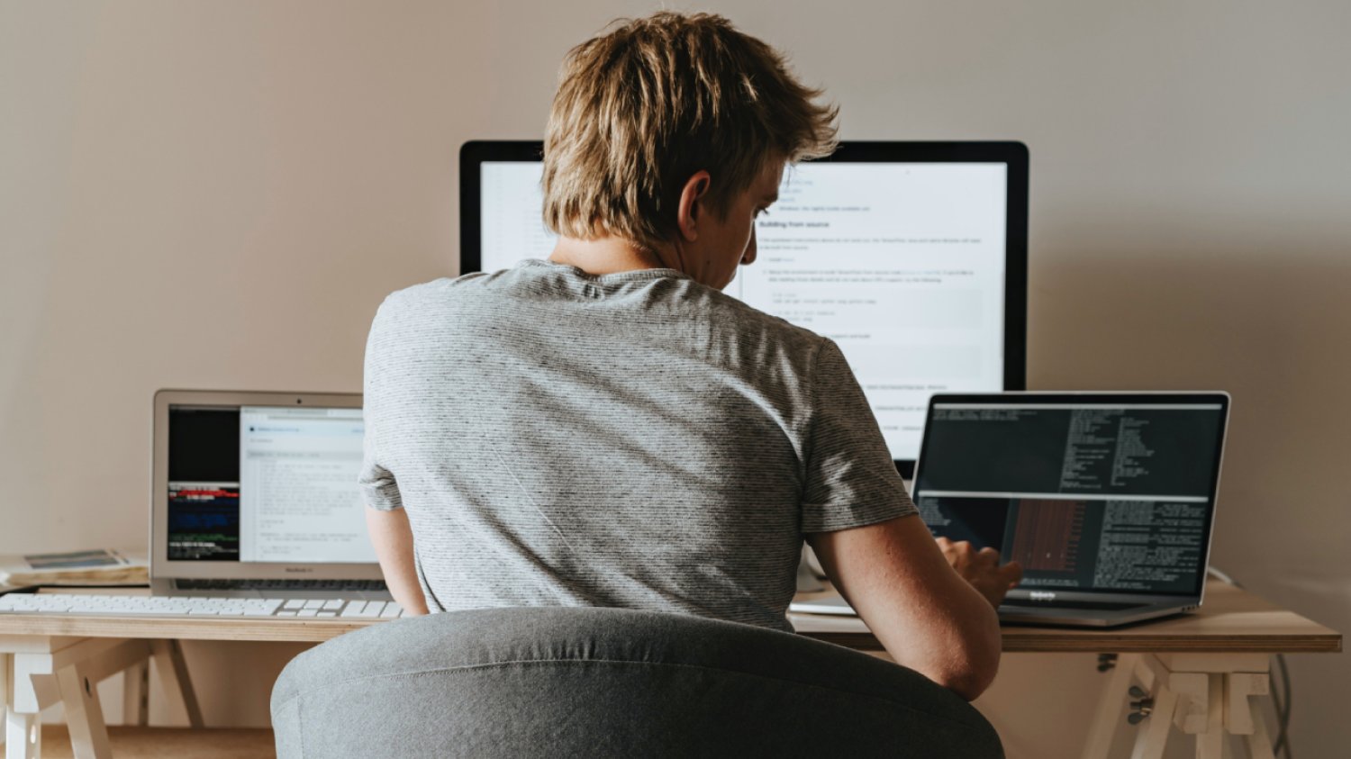 programista siedzący przed trzema monitorami