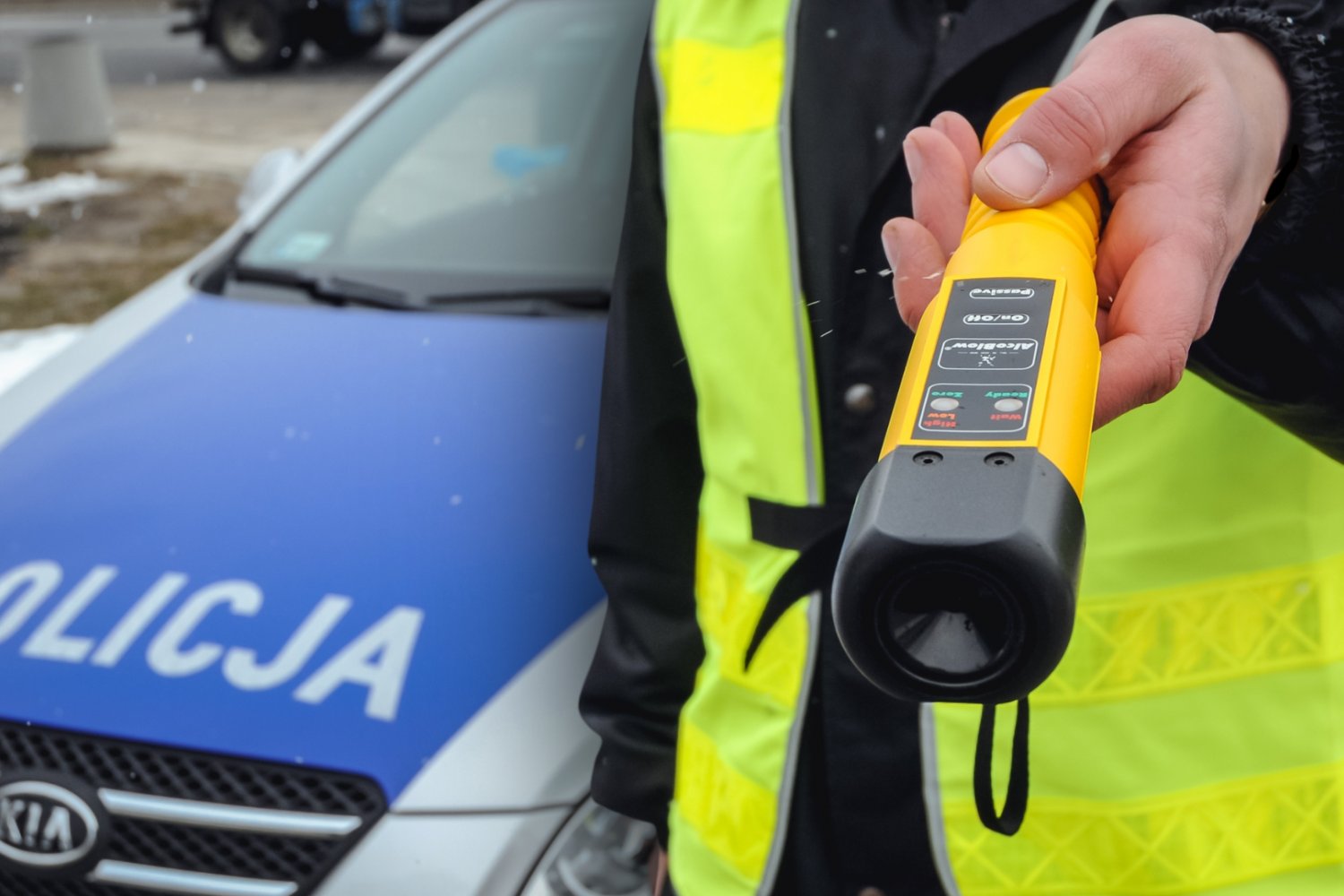 Policjant z alkomatem. W tle samochód policyjny